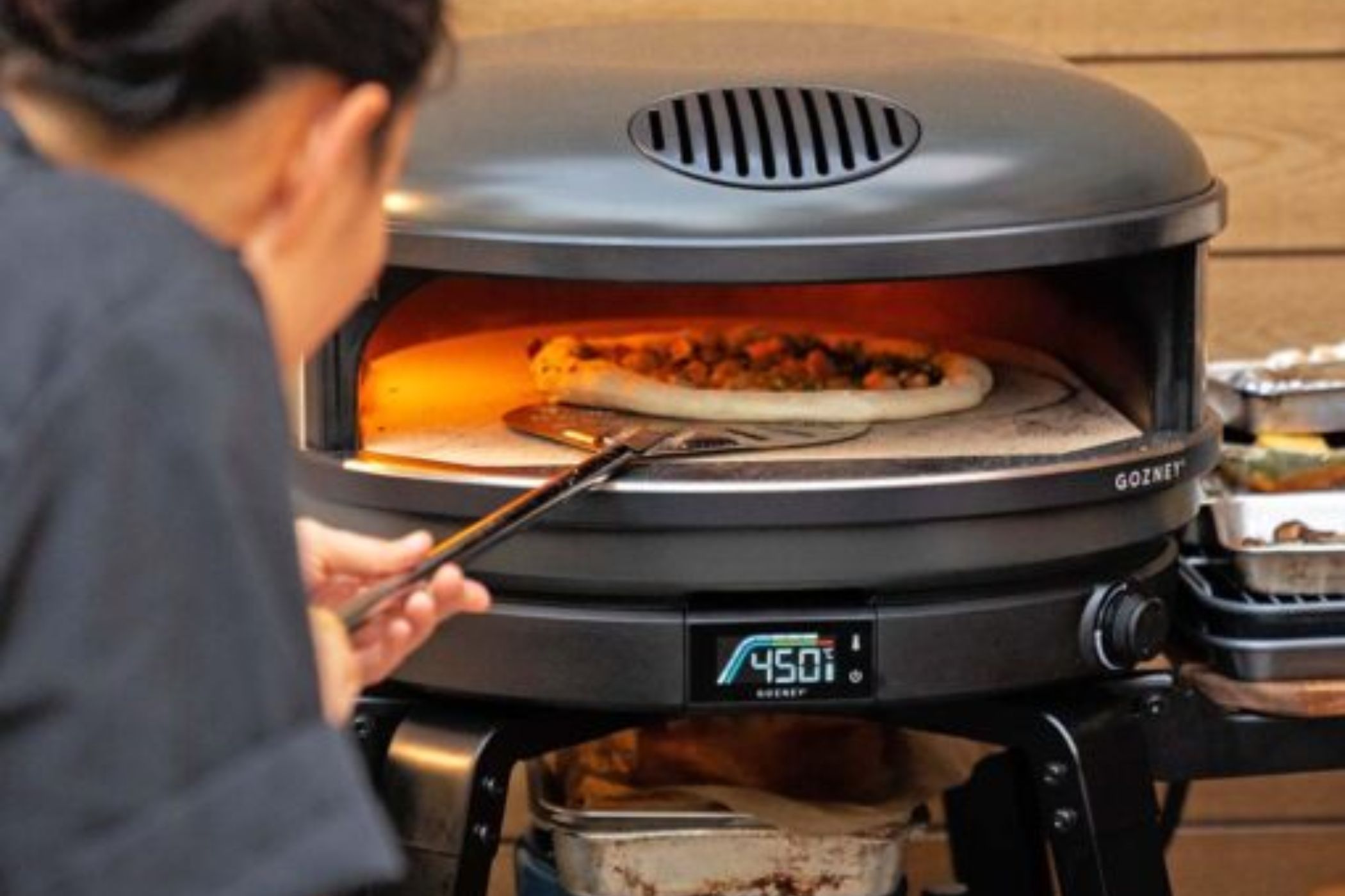 Person sliding pizza into pizza oven on peel